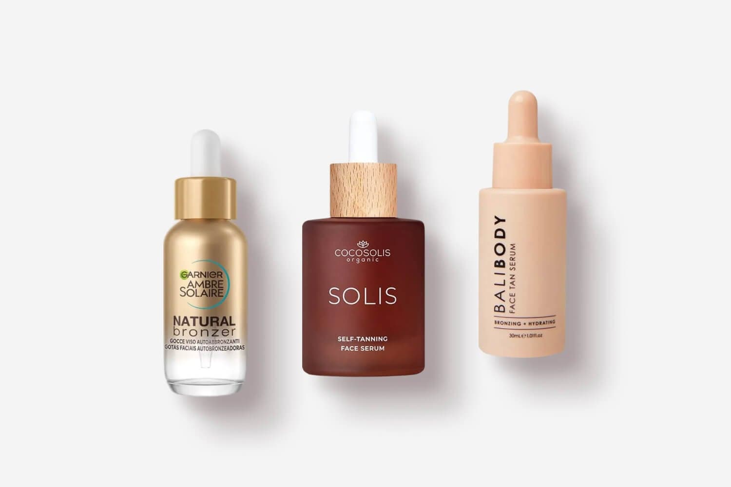 Garnier Ambre Solaire Natural Bronzer drops, Cocosolis Solis Self-Tanning Face Serum and Bali Body Face Tan Serum on grey. Garnier Ambre Solaire Natural Bronzer drops, Cocosolis Solis Self-Tanning Face Serum and Bali Body Face Tan Serum on grey.