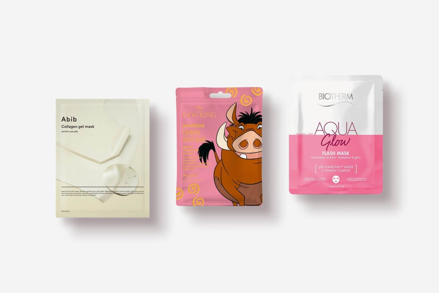 Three sachets on grey: Abib Collagen Gel Mask Jericho Rose Jelly, Lion King Pumbaa sheet mask, and Biotherm Aqua Glow Flash Mask. Three sachets on grey: Abib Collagen Gel Mask Jericho Rose Jelly, Lion King Pumbaa sheet mask, and Biotherm Aqua Glow Flash Mask.