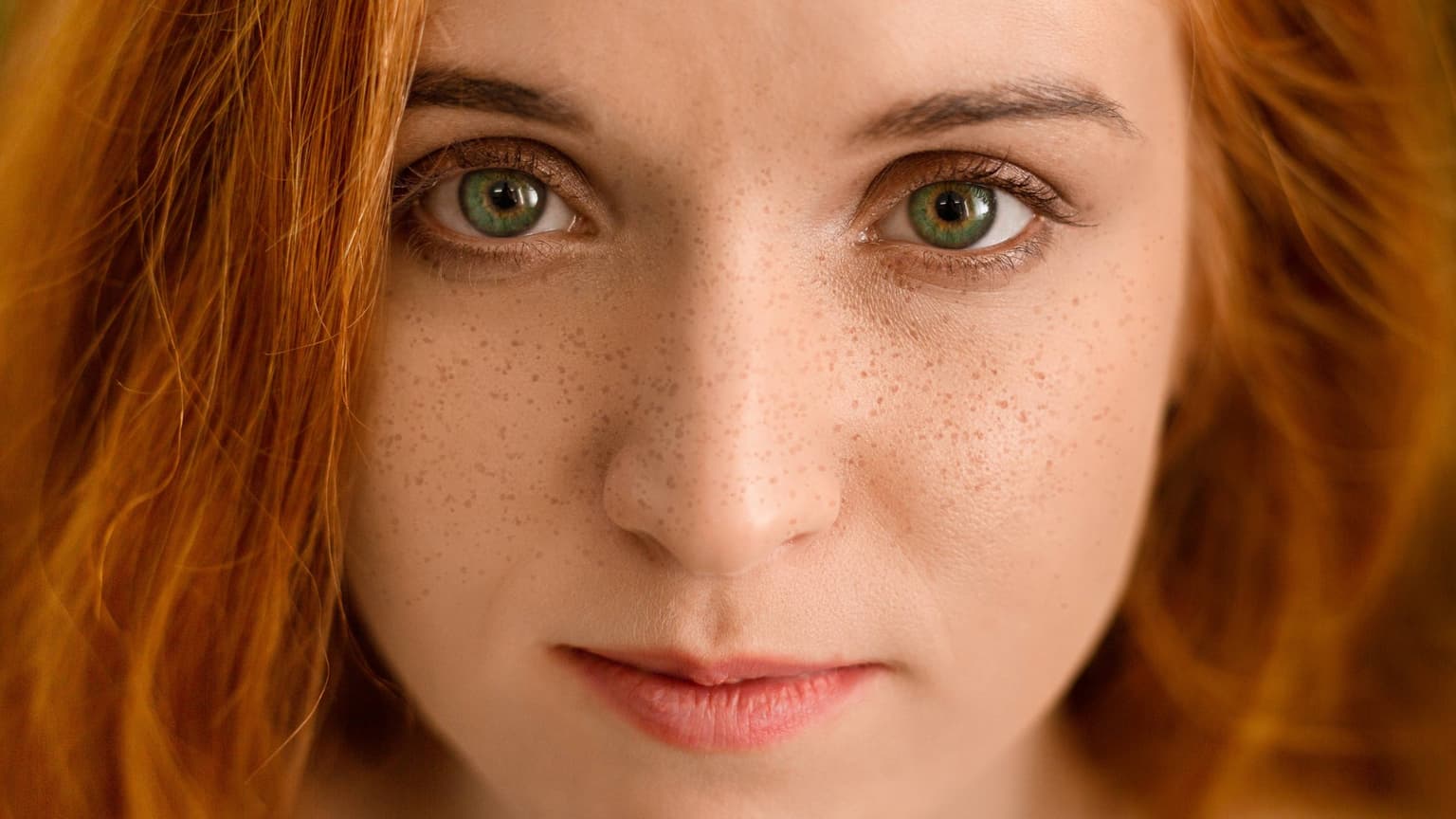 Close-up of a red-haired, green-eyed person with freckles scattered across the nose and cheeks. Close-up of a red-haired, green-eyed person with freckles scattered across the nose and cheeks.