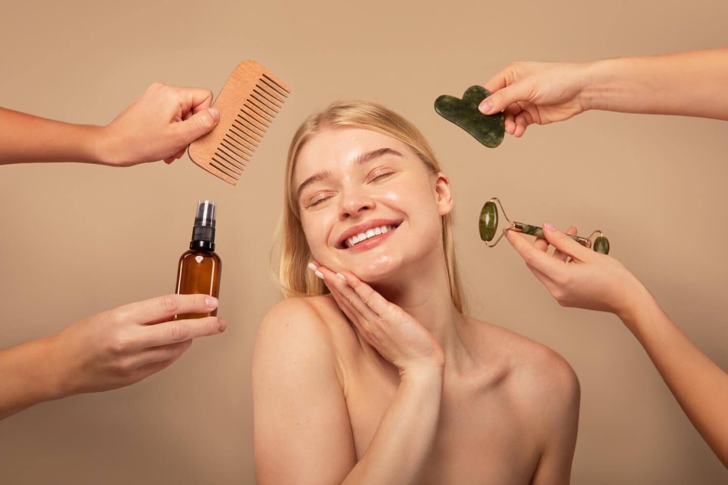 Smiling woman surrounded by hands holding a wooden comb, amber glass spray bottle, jade gua sha stone and jade face roller. Smiling woman surrounded by hands holding a wooden comb, amber glass spray bottle, jade gua sha stone and jade face roller.