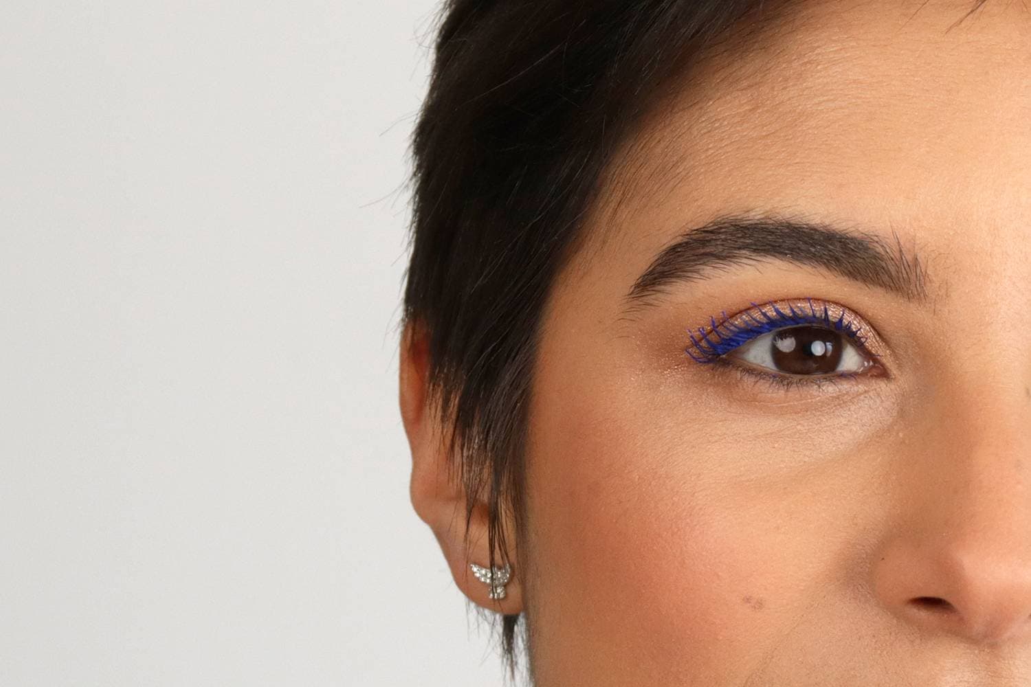 Close-up of a brown eye with electric blue mascara on the upper lashes over warm copper shimmer shadow and a groomed brow. Close-up of a brown eye with electric blue mascara on the upper lashes over warm copper shimmer shadow and a groomed brow.