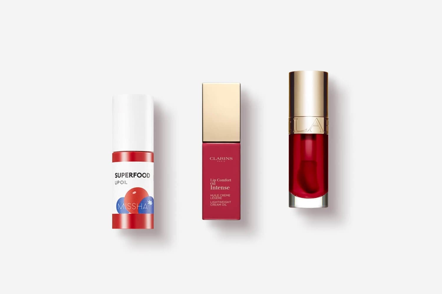 Missha Superfood Lip Oil beside Clarins Lip Comfort Oil Intense in its box and a red gold-capped bottle.