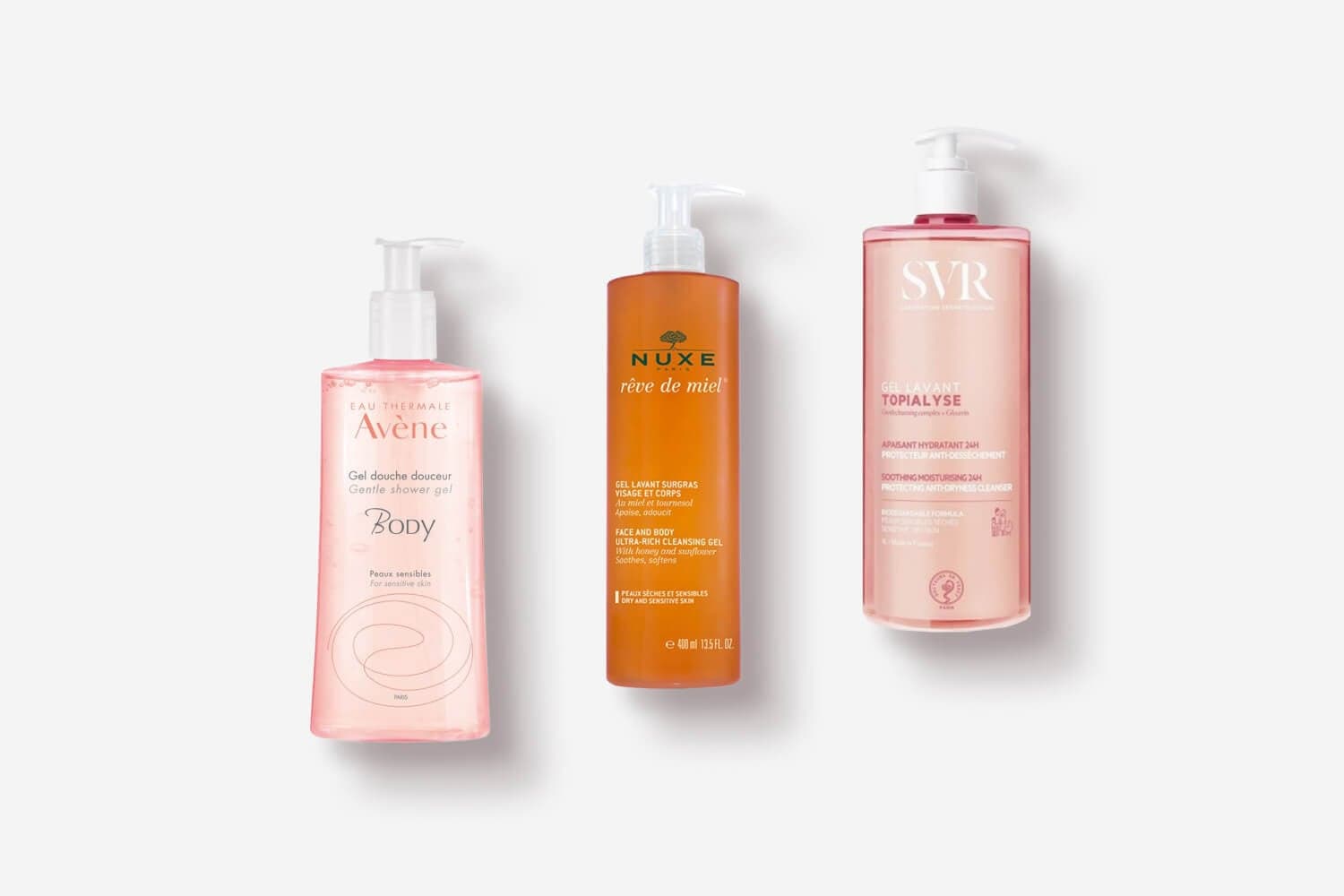 Avène Body Gentle Shower Gel, Nuxe Rêve de Miel cleansing gel and SVR Topialyse Gel Lavant pump bottles on grey. Avène Body Gentle Shower Gel, Nuxe Rêve de Miel cleansing gel and SVR Topialyse Gel Lavant pump bottles on grey.