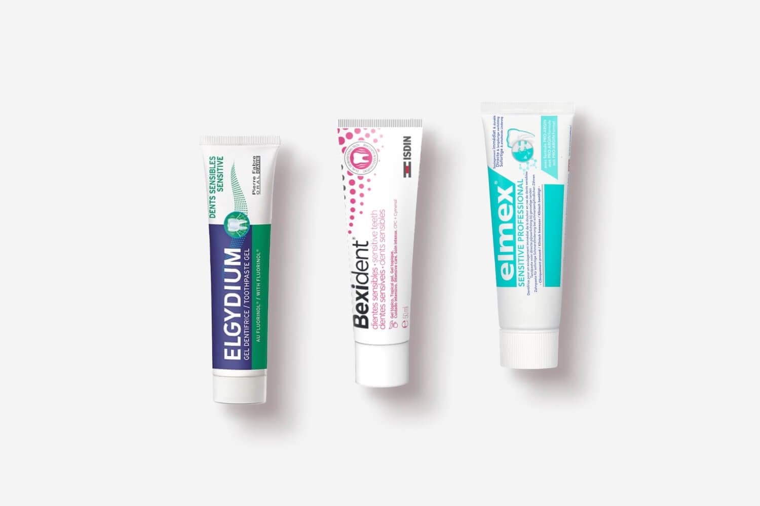 Three toothpaste tubes on grey: Elgydium Sensitive gel, Isdin Bexident Sensitive Teeth and Elmex Sensitive Professional. Three toothpaste tubes on grey: Elgydium Sensitive gel, Isdin Bexident Sensitive Teeth and Elmex Sensitive Professional.