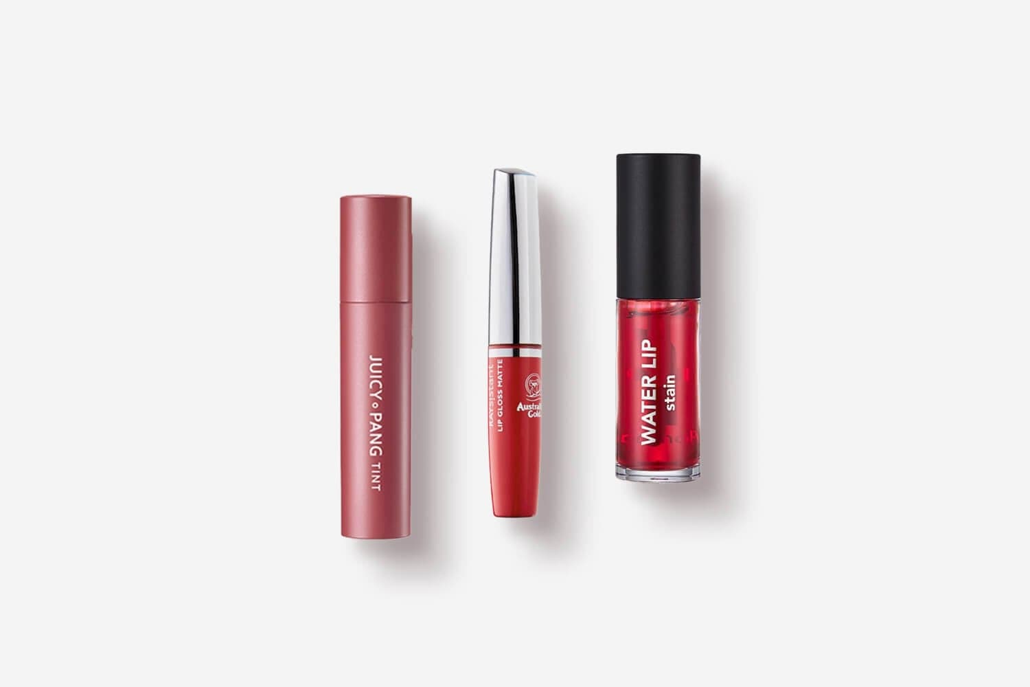 Juicy Pang Tint, Australian Gold Lip Gloss Matte and a red Water Lip Stain lined up on a pale grey background. Juicy Pang Tint, Australian Gold Lip Gloss Matte and a red Water Lip Stain lined up on a pale grey background.