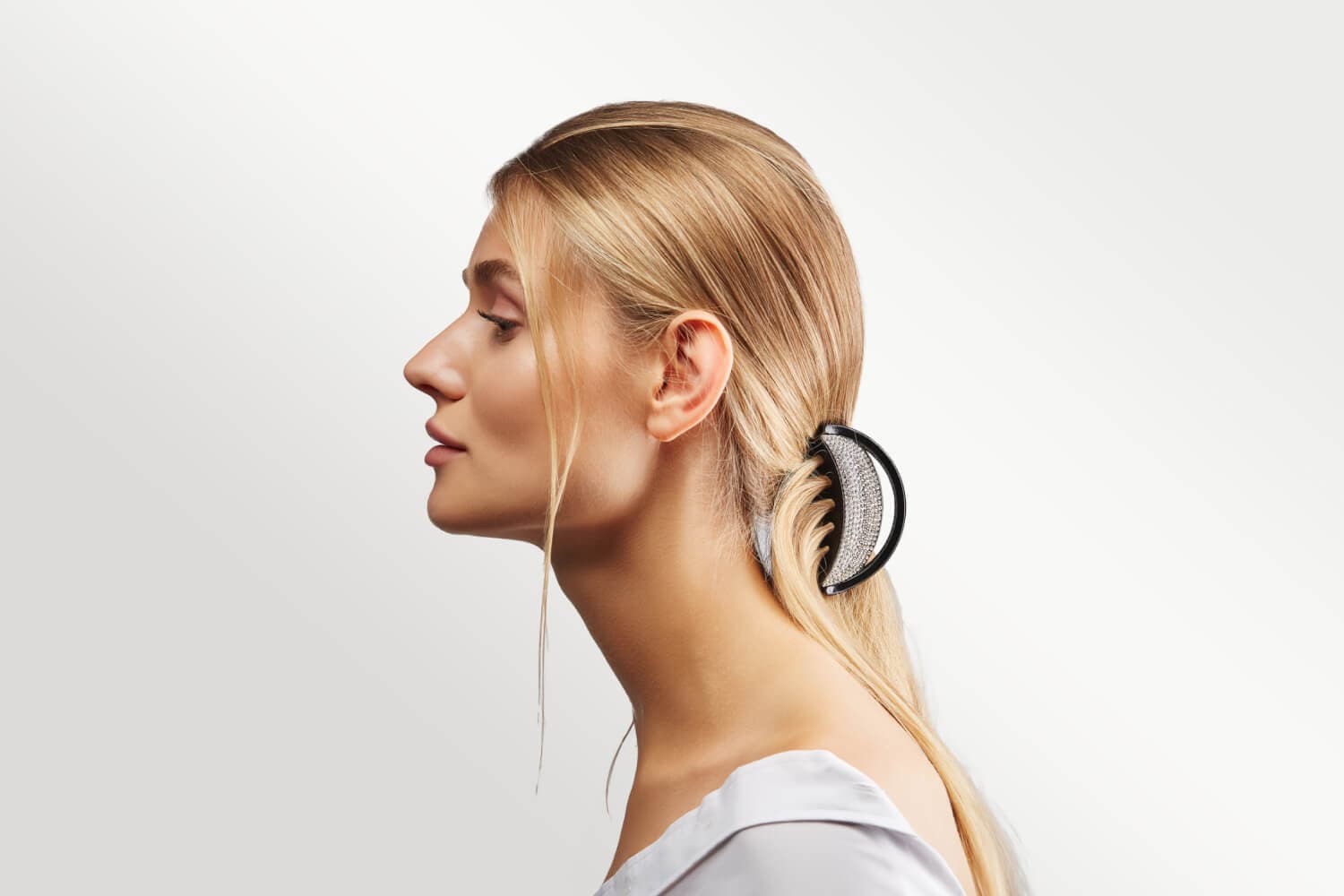Side profile of a blonde woman with her long hair swept back and held by a black rhinestone-studded banana clip. Side profile of a blonde woman with her long hair swept back and held by a black rhinestone-studded banana clip.