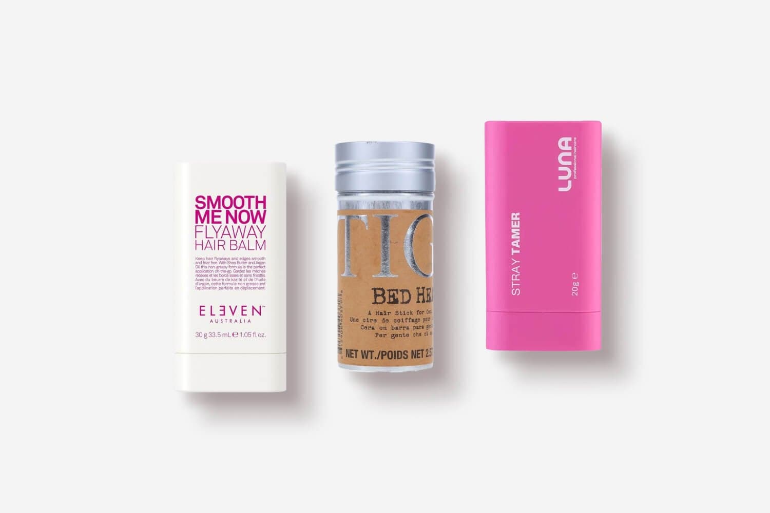 Eleven Australia Smooth Me Now Flyaway Hair Balm, TIGI Bed Head hair stick and pink Luna Stray Tamer stick on white. Eleven Australia Smooth Me Now Flyaway Hair Balm, TIGI Bed Head hair stick and pink Luna Stray Tamer stick on white.