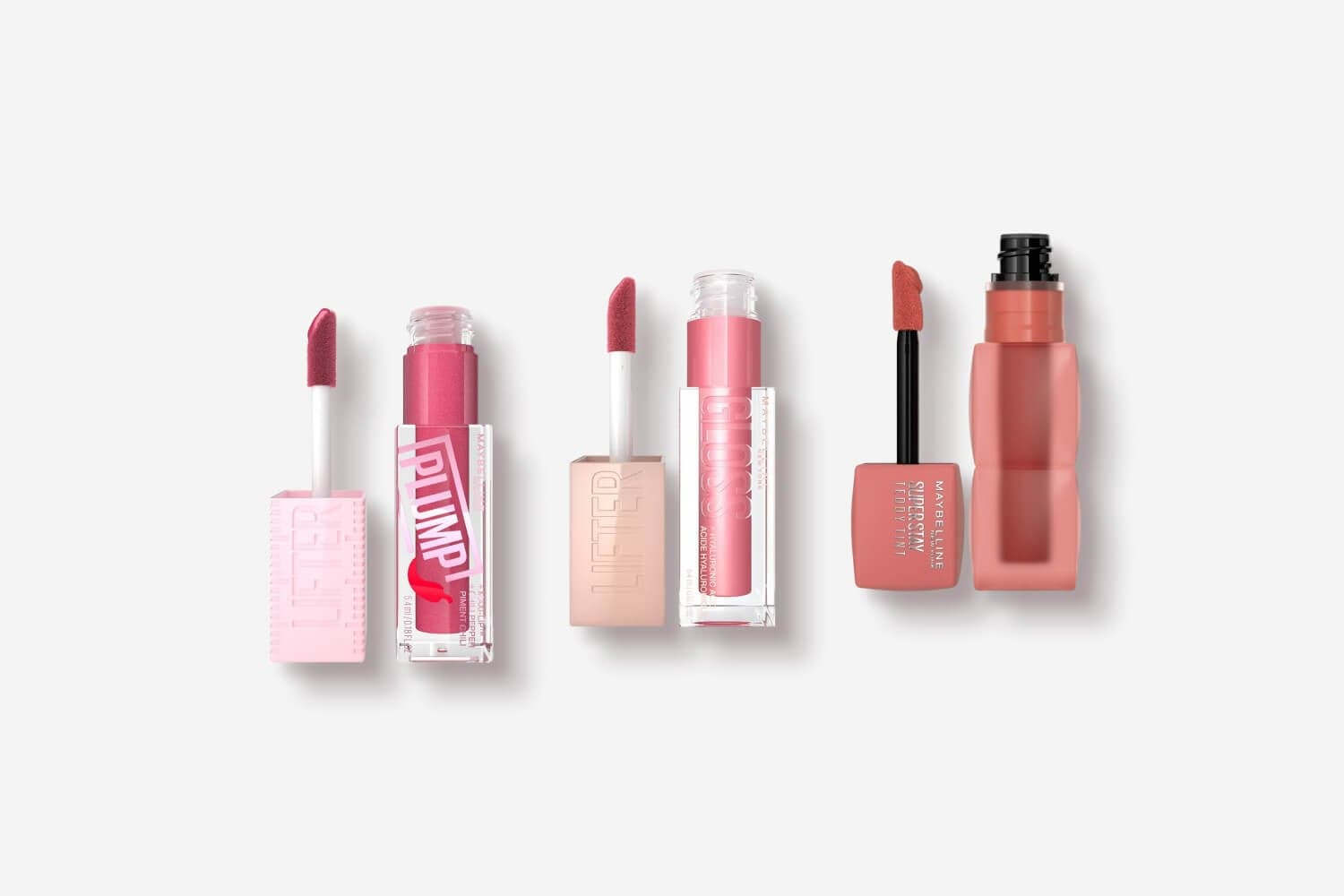 Three open Maybelline lip products on grey: Lifter Plump in berry pink, Lifter Gloss in soft pink and SuperStay Teddy Tint in nude. Three open Maybelline lip products on grey: Lifter Plump in berry pink, Lifter Gloss in soft pink and SuperStay Teddy Tint in nude.